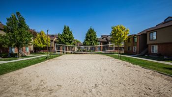 A sandy area in front of apartment buildings with trees and a volleyball net.